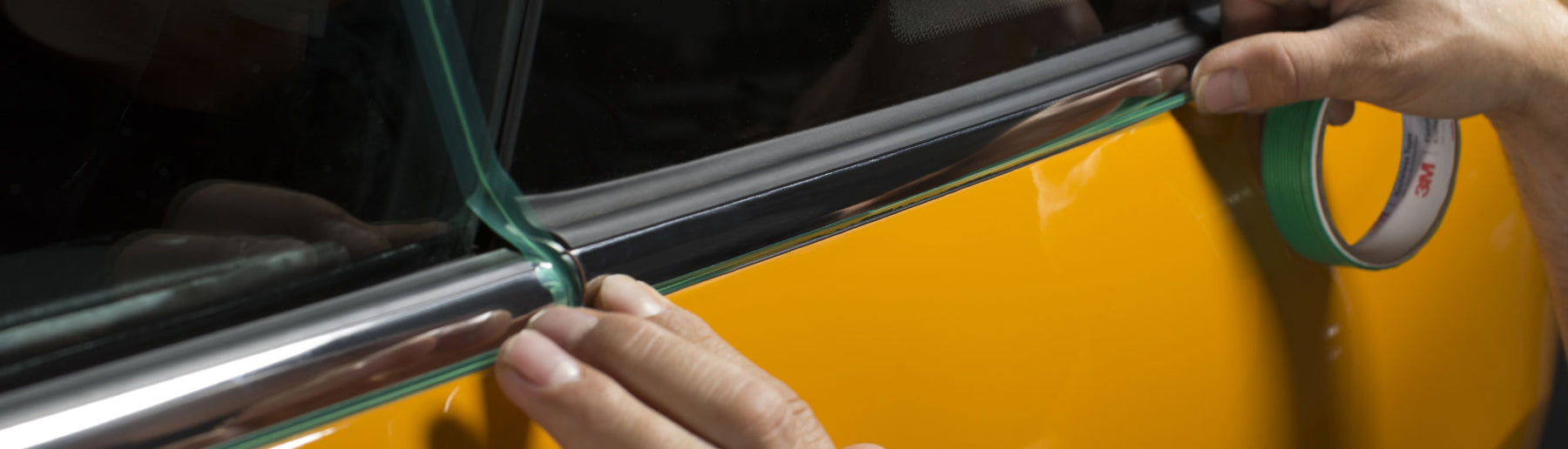 Man's hand pressing green knifeless tape into a yellow and black vehicle door