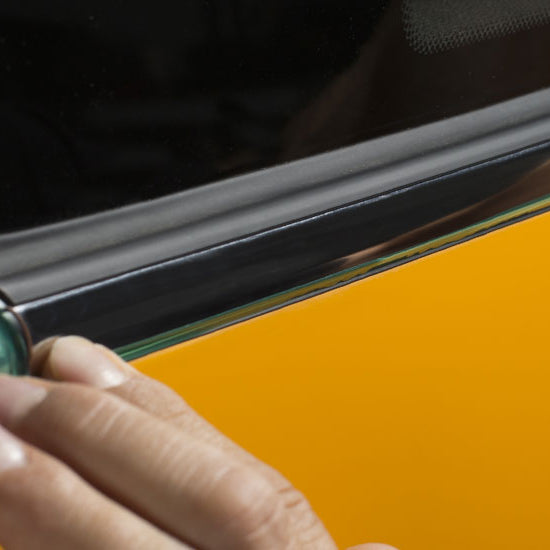 Man's hand pressing green knifeless tape into a yellow and black vehicle door